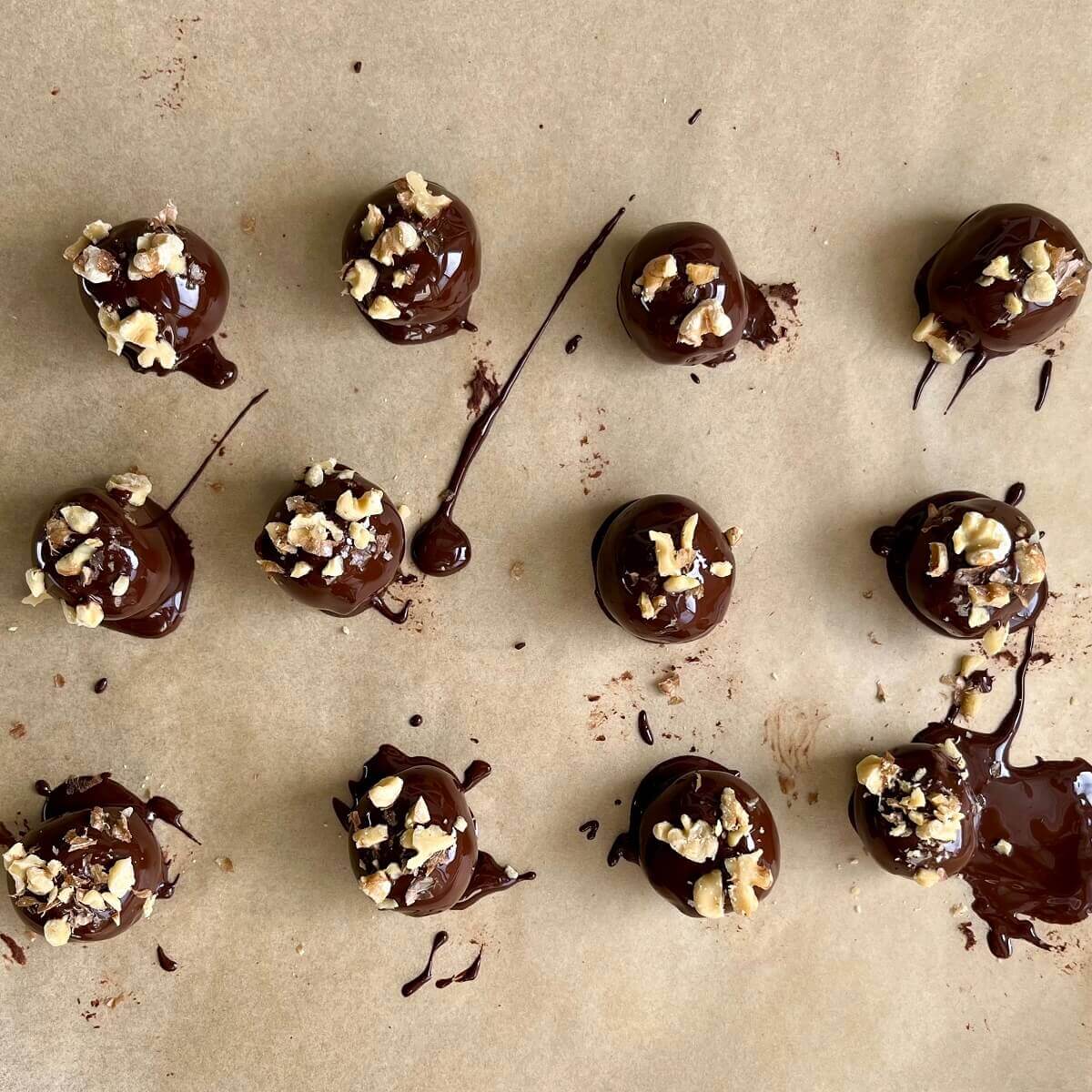 Chocolate coated banana balls sprinkled with chopped walnuts on a piece of parchment paper.