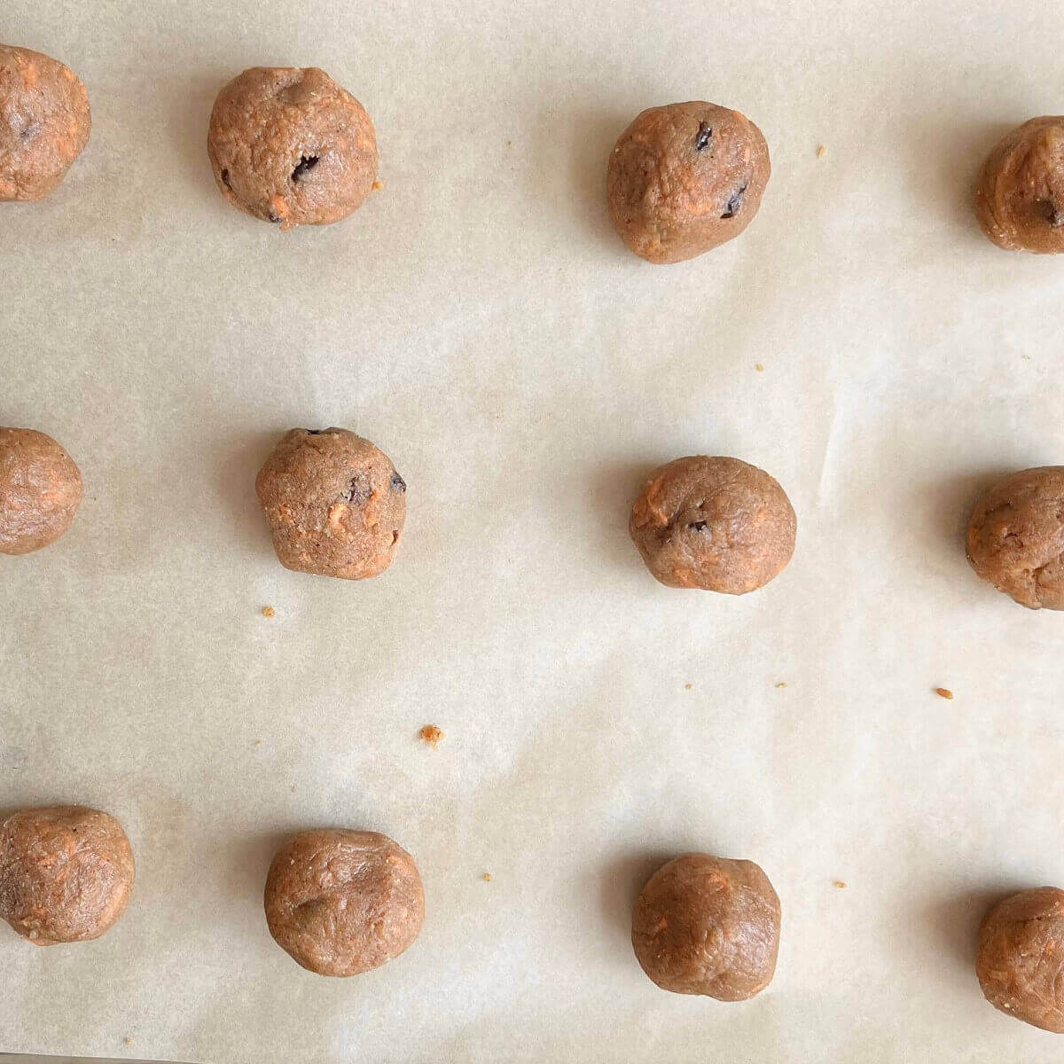 Carrot cookie dough balls on a baking sheet lined with parchment paper.