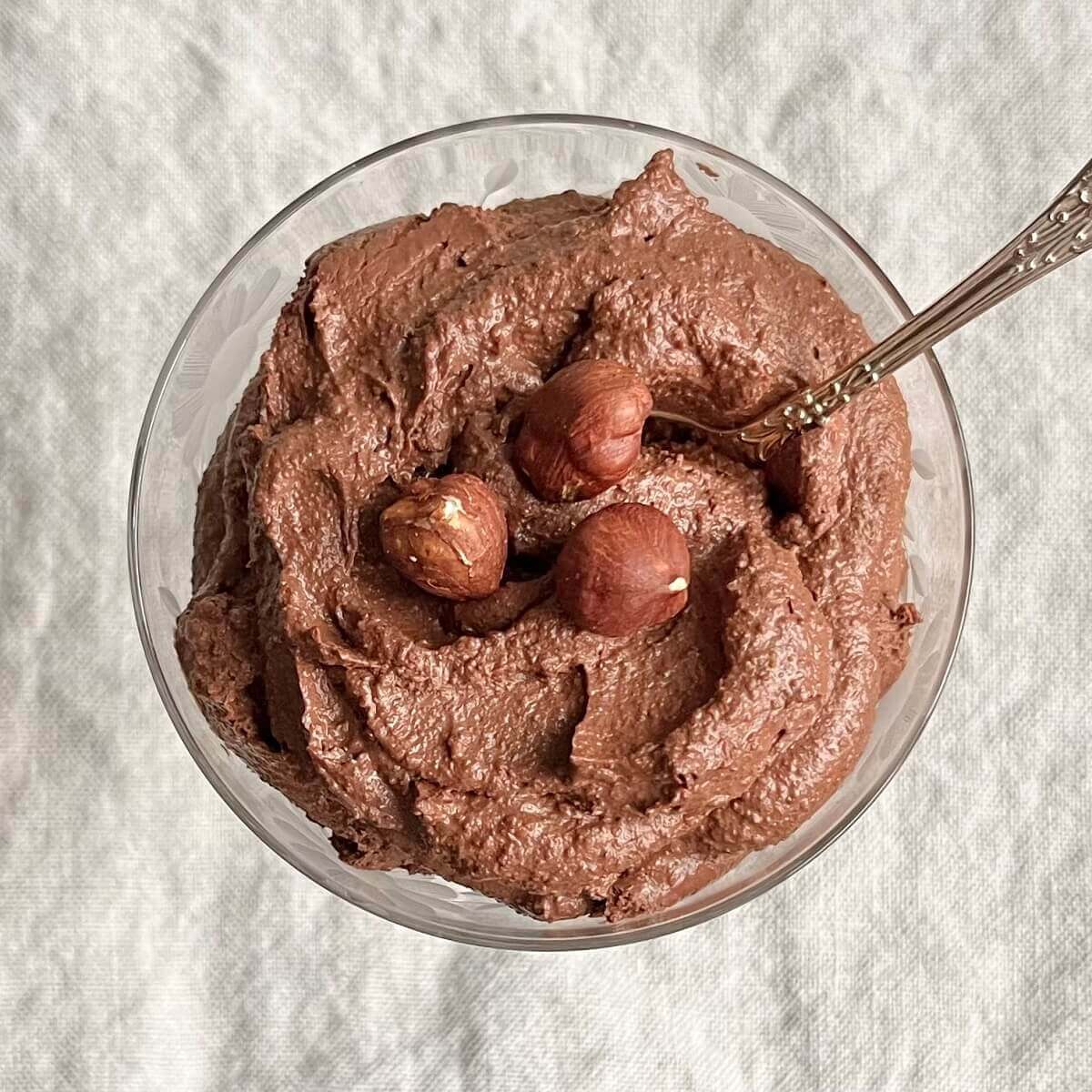 A glass dish of chocolate hazelnut mousse with three hazelnuts on top.