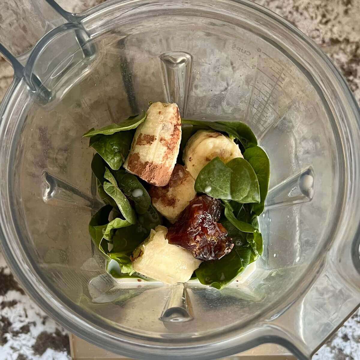 Spinach leaves, banana, a date, cocoa powder, and almond milk in a blender.