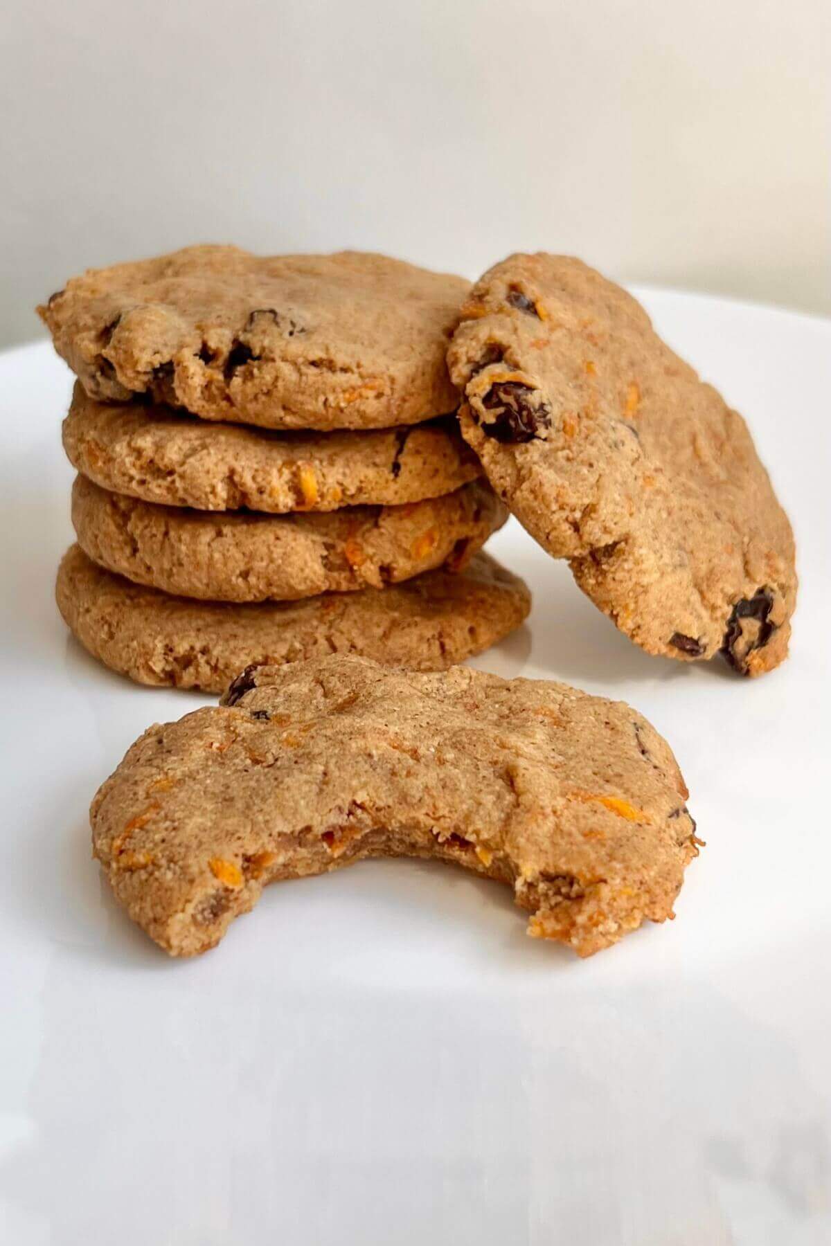 Vegan carrot cookies on a white plate with a bite missing from one.