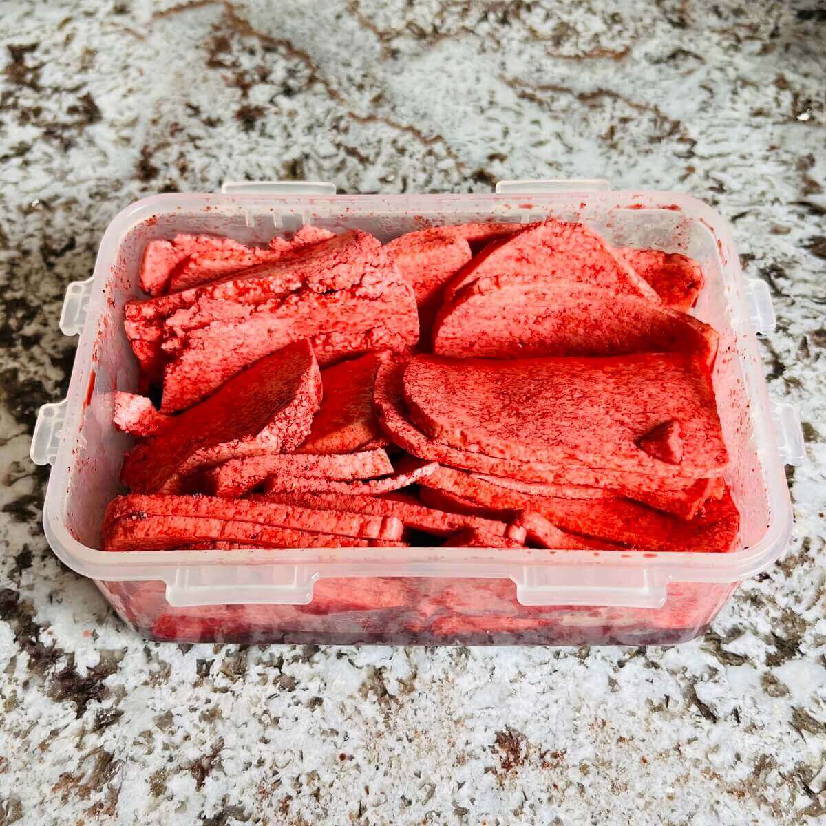 Vegan corned beef marinating in a plastic container.