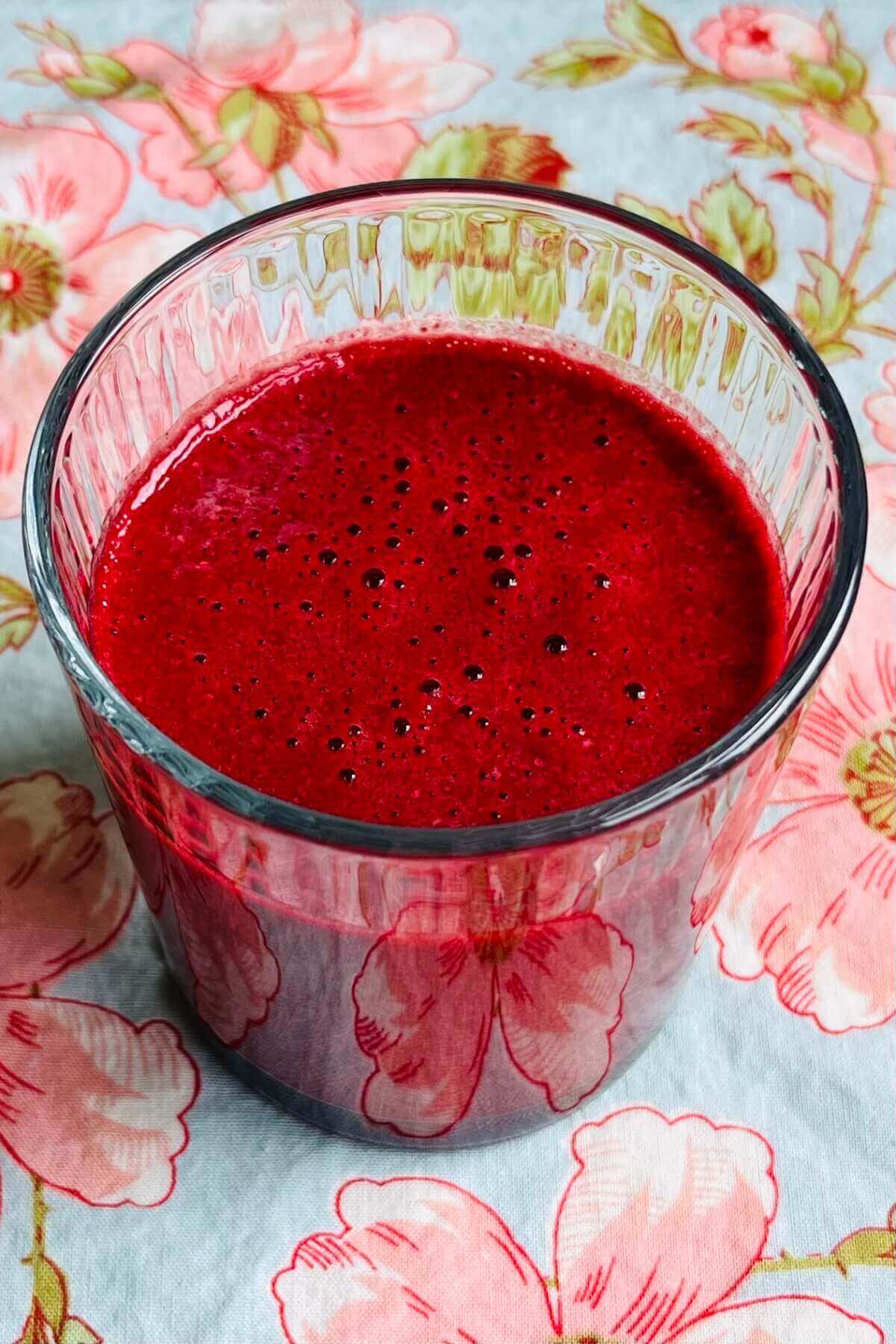 A beet smoothie in a glass on a floral placemat.