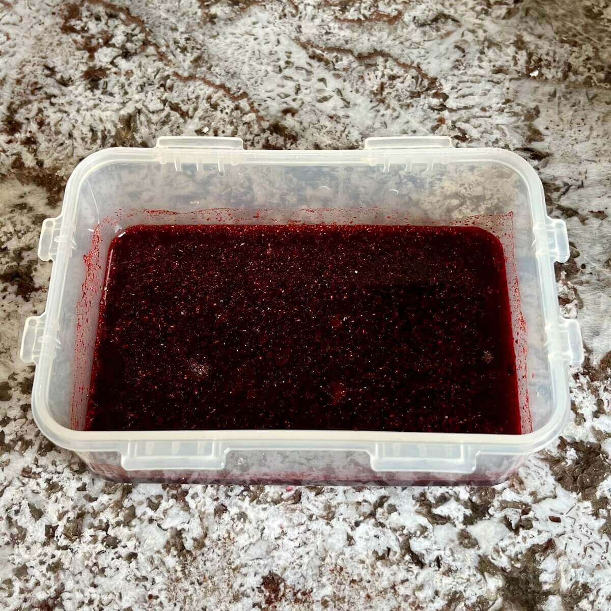 Dark pink marinade in a plastic container.