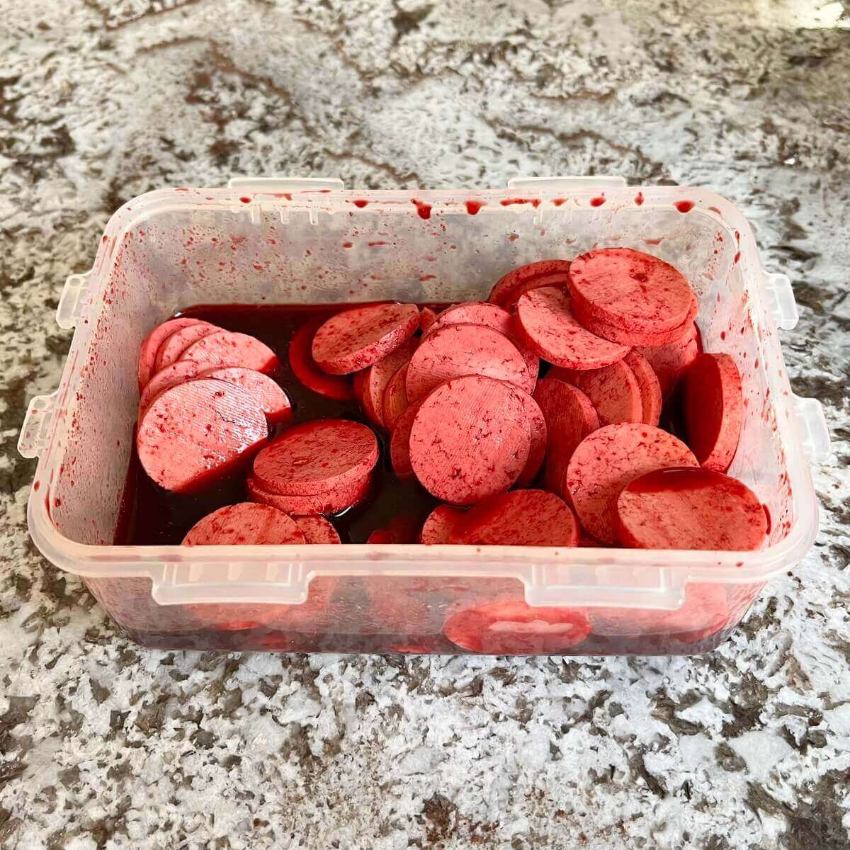 Vegan pepperoni marinating in a plastic container.