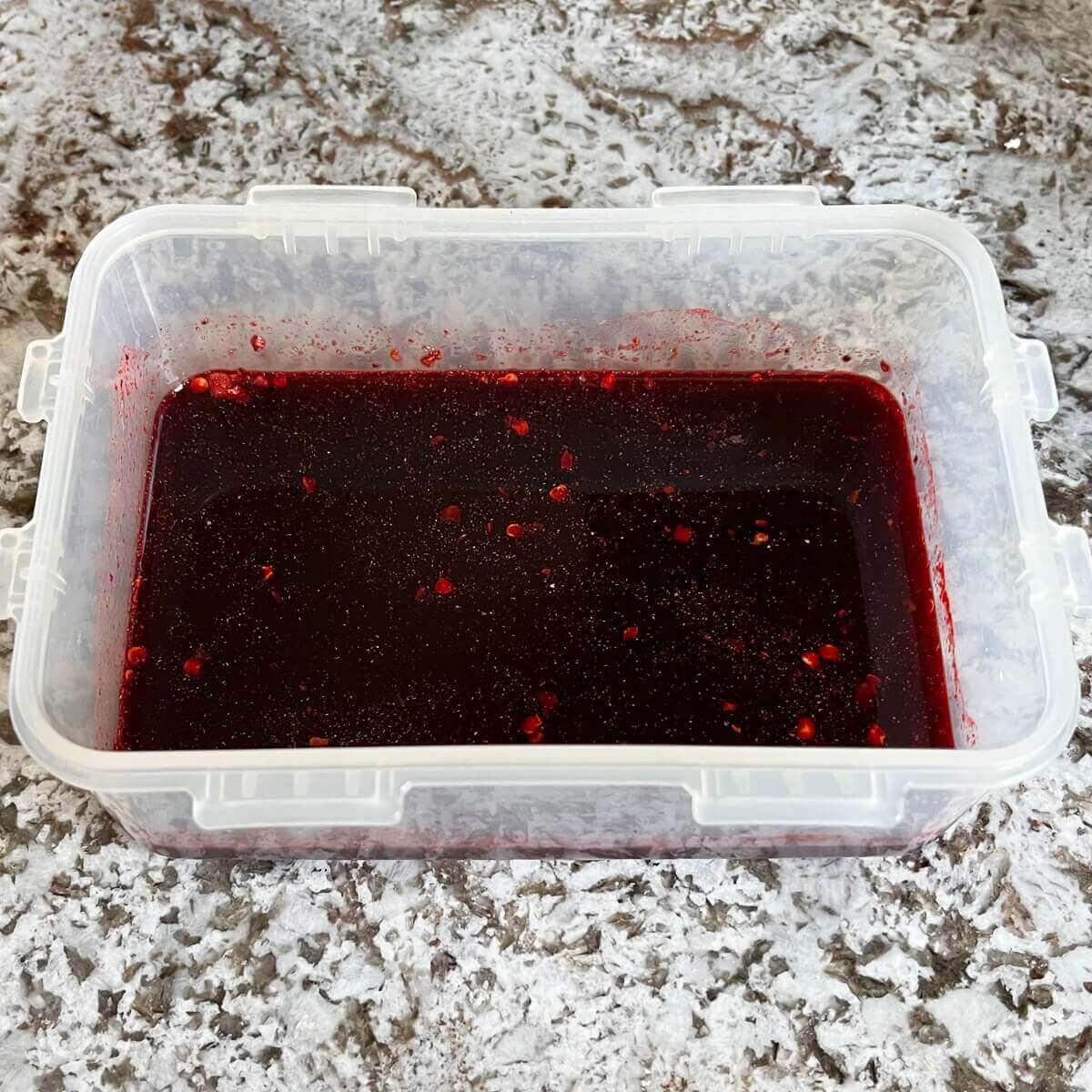 Dark pink marinade for pepperoni in a plastic container.