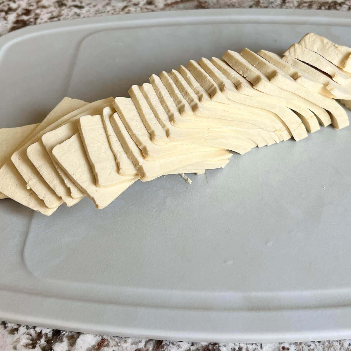 Thin slices of tofu on a cutting board.