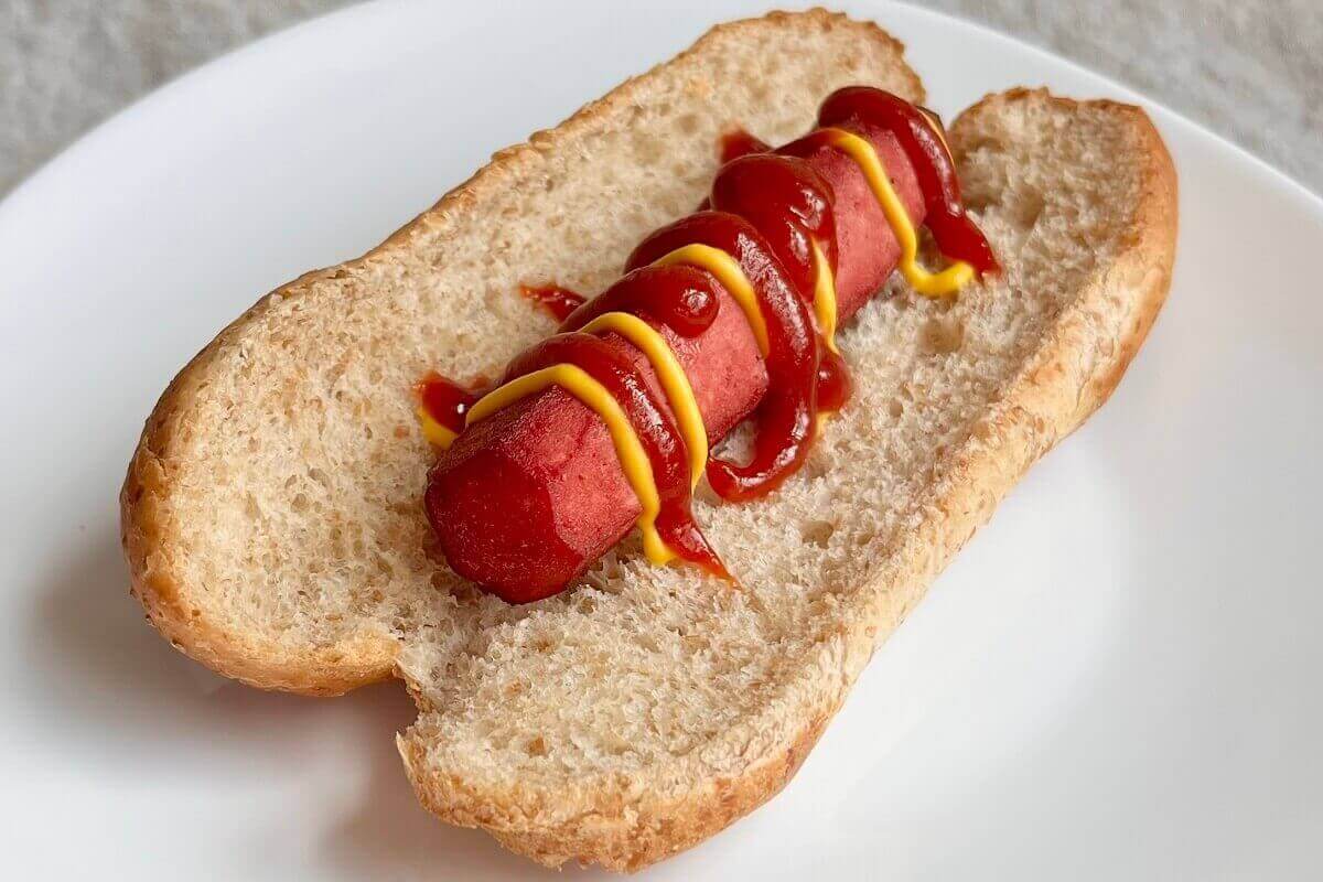 A tofu dog in a bun on a white plate.