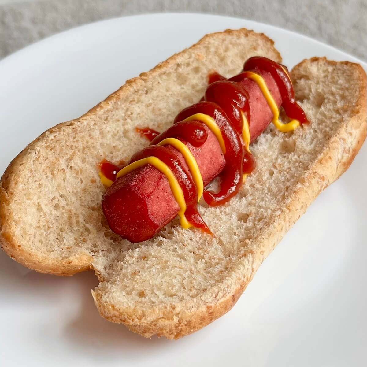 A tofu hot dog in a bun drizzled with ketchup and mustard.