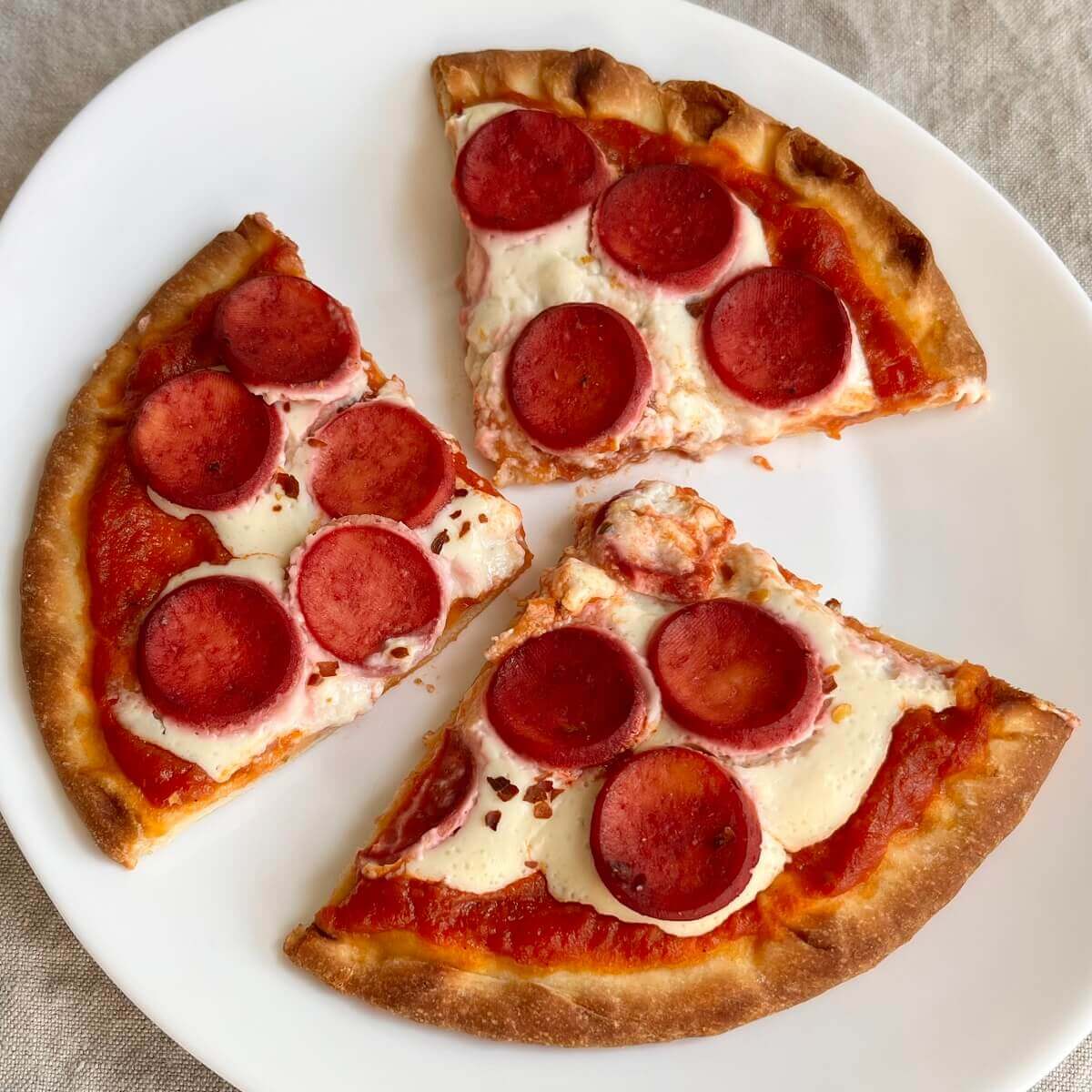 Three slices of tofu pepperoni pizza on a white plate.