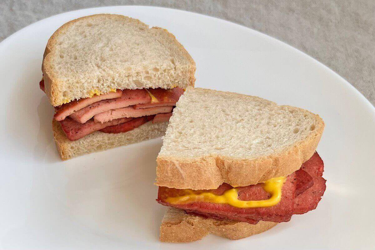 A vegan deli meat sandwich on a white plate.