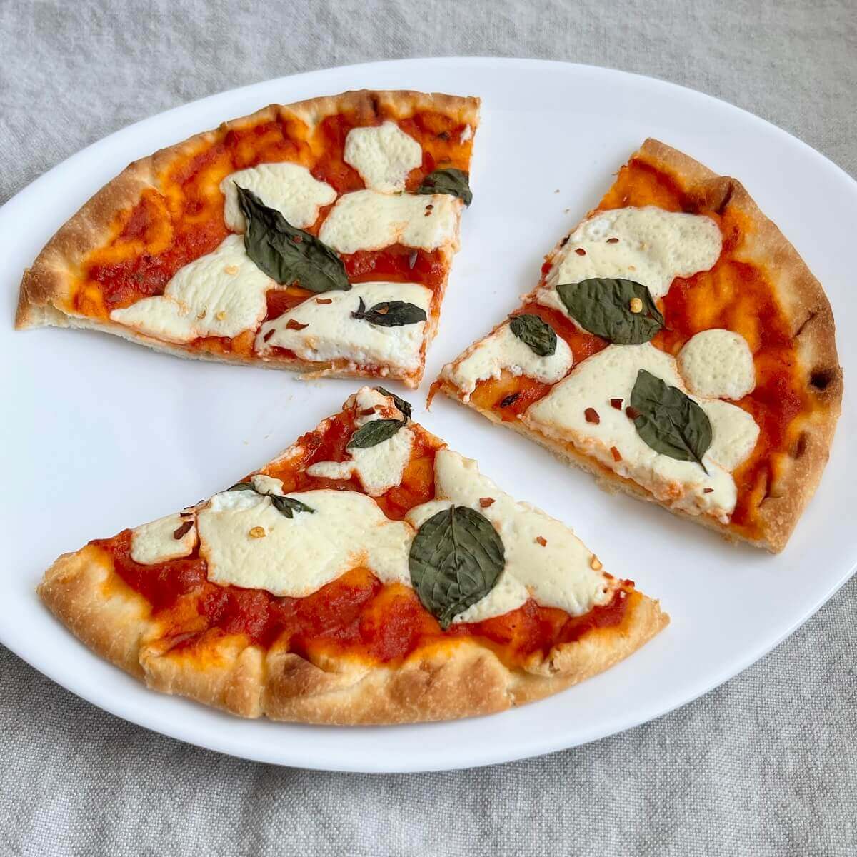 A pizza with vegan liquid mozzarella, tomato sauce, and basil leaves.