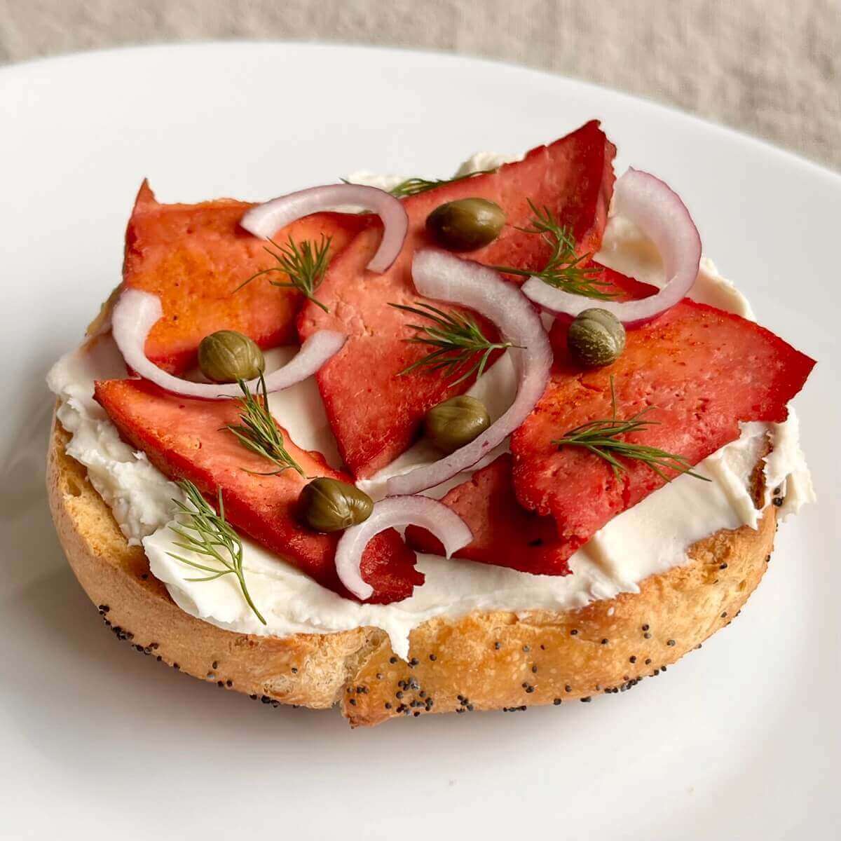 Tofu smoked salmon on a bagel with cream cheese, sliced red onion, fresh dill, and capers.