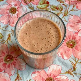 A chocolate pineapple smoothie in a glass on a floral placemat.