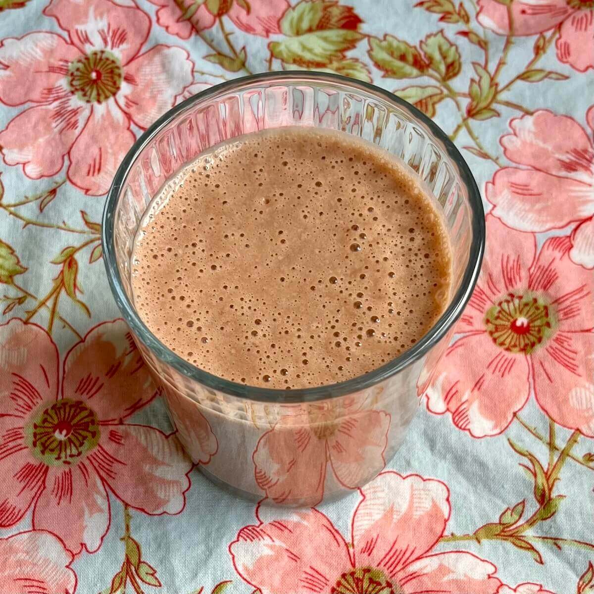 A chocolate pineapple smoothie in a glass on a floral placemat.