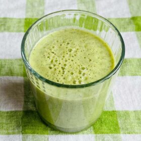 A cucumber kiwi smoothie in a glass on a green gingham placemat.