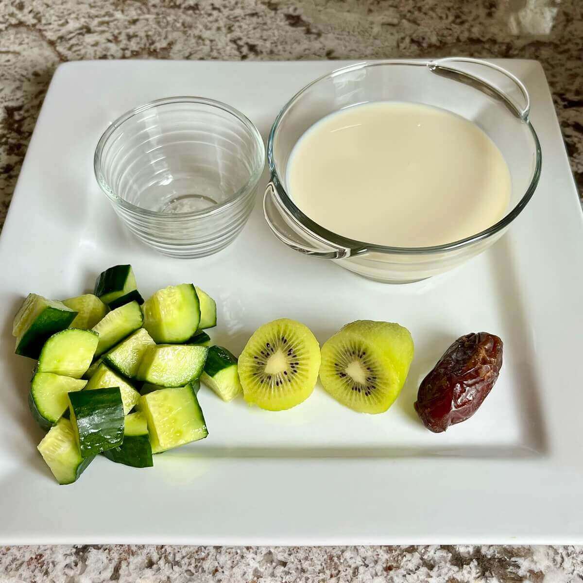 Chopped cucumber, a kiwi, a date, and bowls of soy milk and sea salt on a platter.