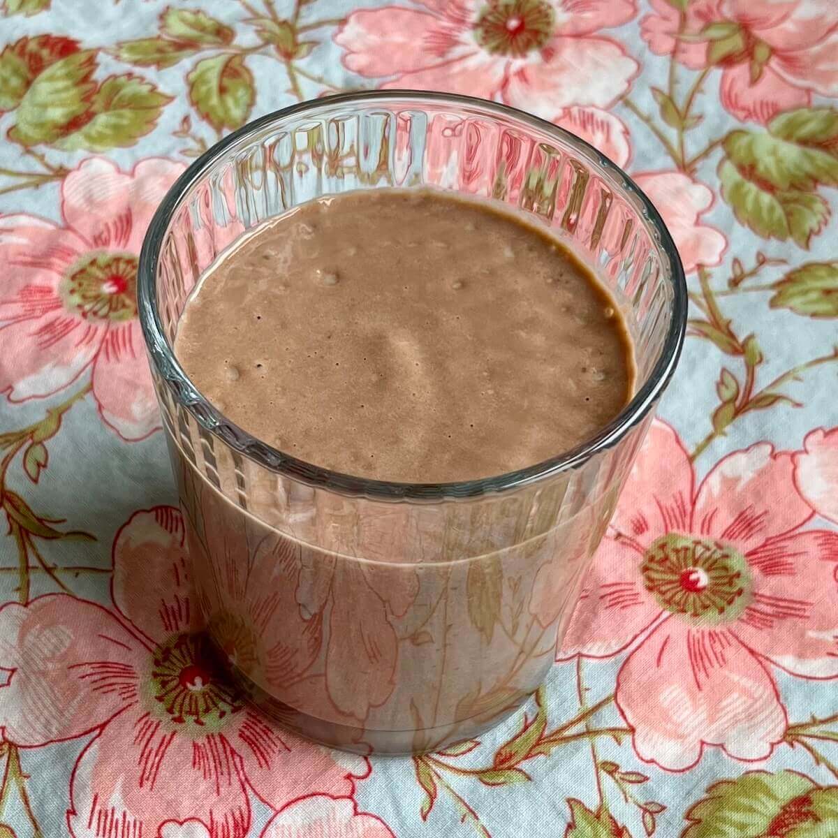 A date and avocado smoothie in a glass on a floral placemat.