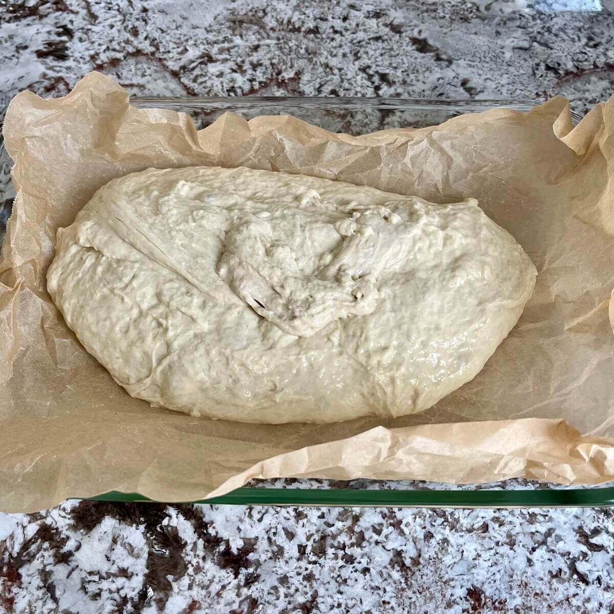 Bread dough in a baking pan lined with parchment paper.