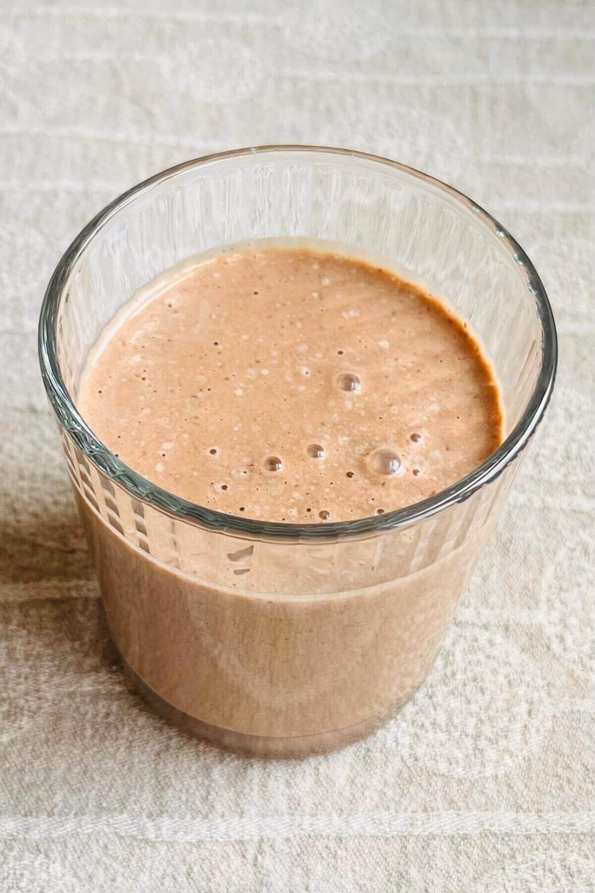 A hazelnut shake in a glass on a beige placemat.
