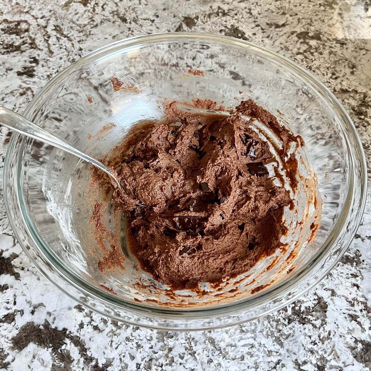 Thick lentil brownie batter in a glass mixing bowl with a spoon.