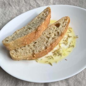 Two slices of artisan bread on a plate with olive oil and rosemary.