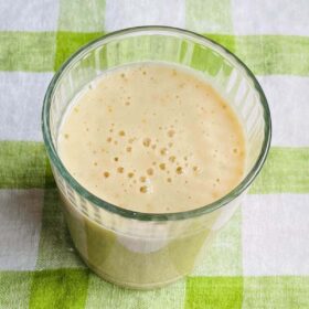 A pear and banana smoothie in a glass on a green gingham cloth.