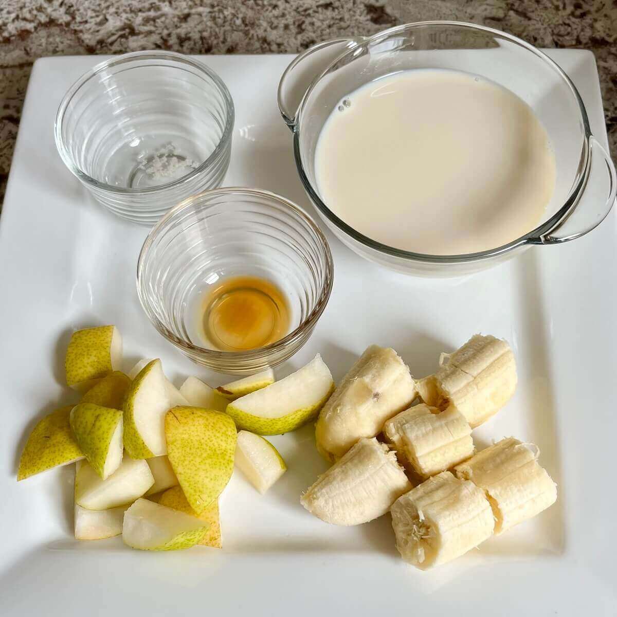 Chopped pears, banana, and bowls of vanilla extract, sea salt, and soy milk on a platter.