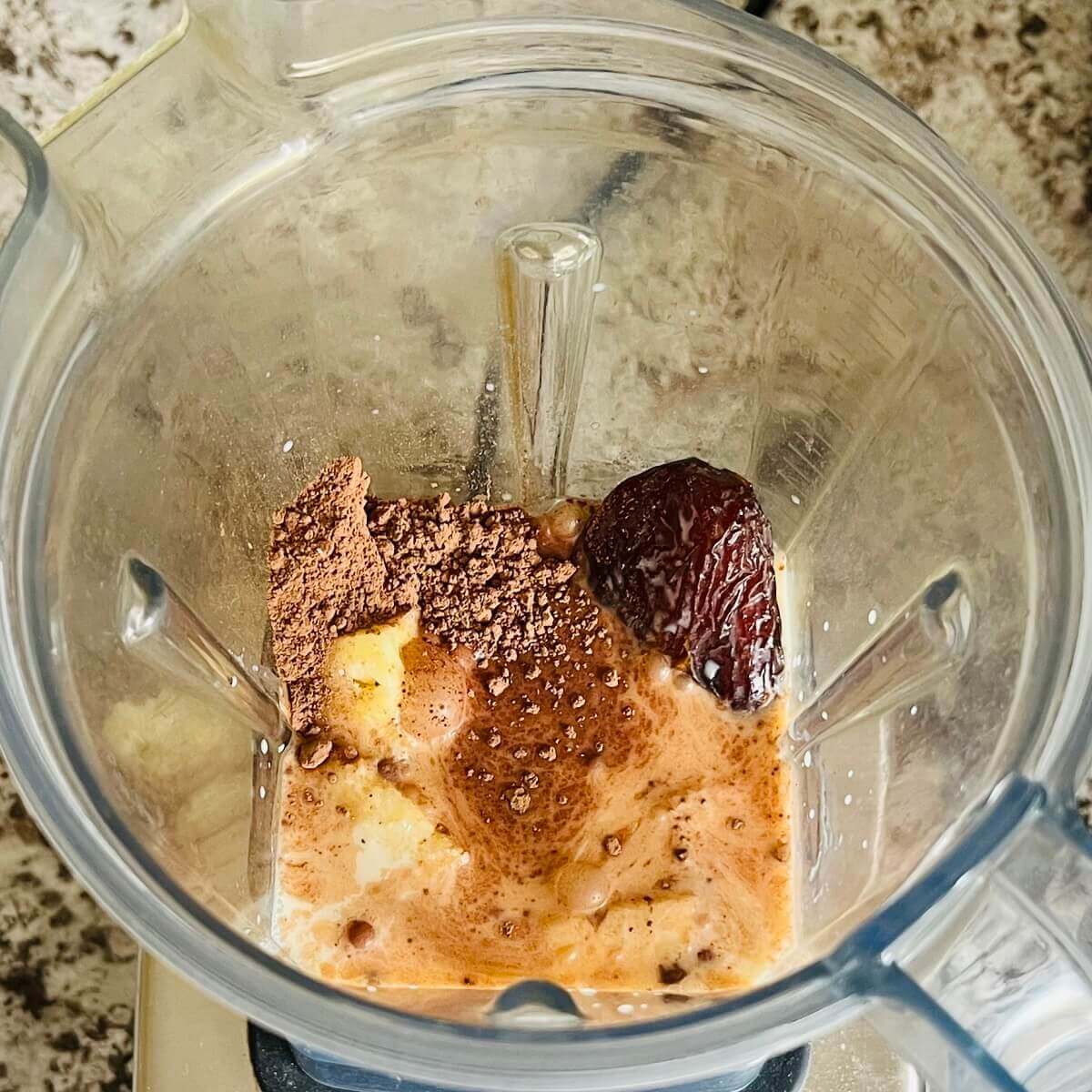 Chopped pineapple, soy milk, cocoa powder, salt, and a date in a blender.