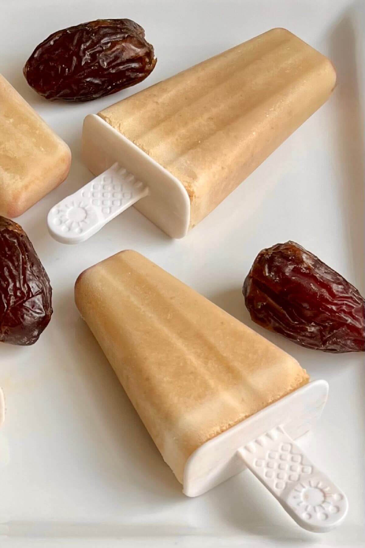 Creamy light brown popsicles and dates on a plate.