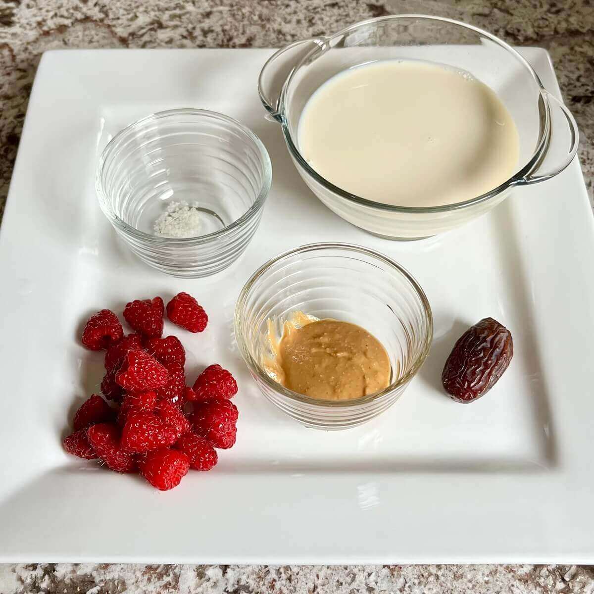 Raspberries, a date, and bowls of peanut butter, sea salt, and soy milk on a platter.