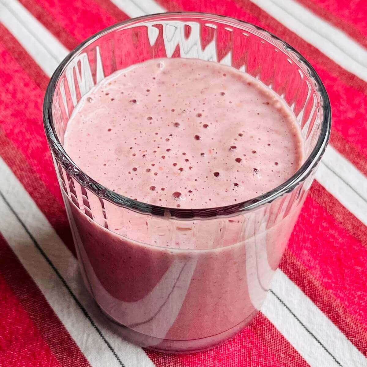 A raspberry peanut butter smoothie in a glass on a striped cloth.