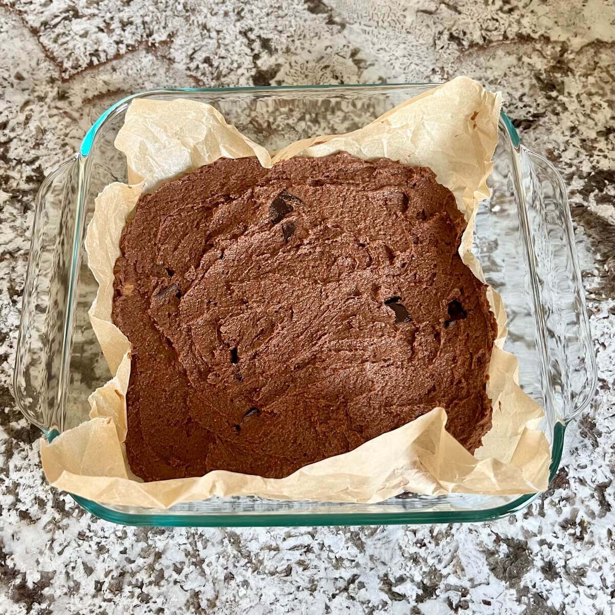 Raw brownies made with lentils in a square baking dish lined with parchment paper.