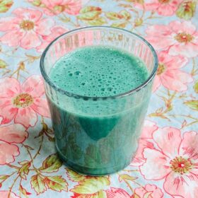 A spirulina banana smoothie in a glass on a floral placemat.