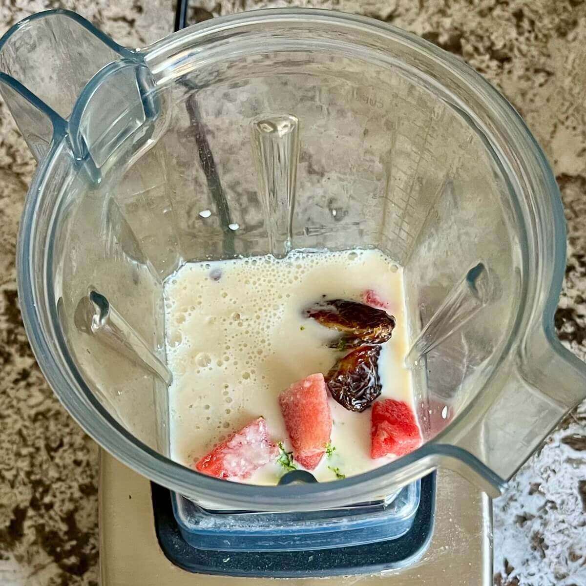 Chopped watermelon, lime, and other ingredients for a smoothie in a blender.