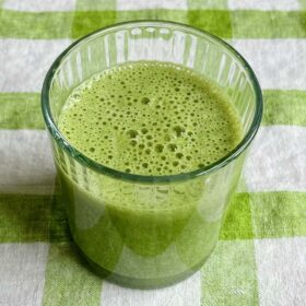 A chlorella smoothie in a glass on a green gingham cloth.
