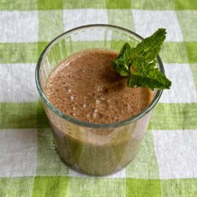 A cocoa mint smoothie in a glass on a green gingham cloth.