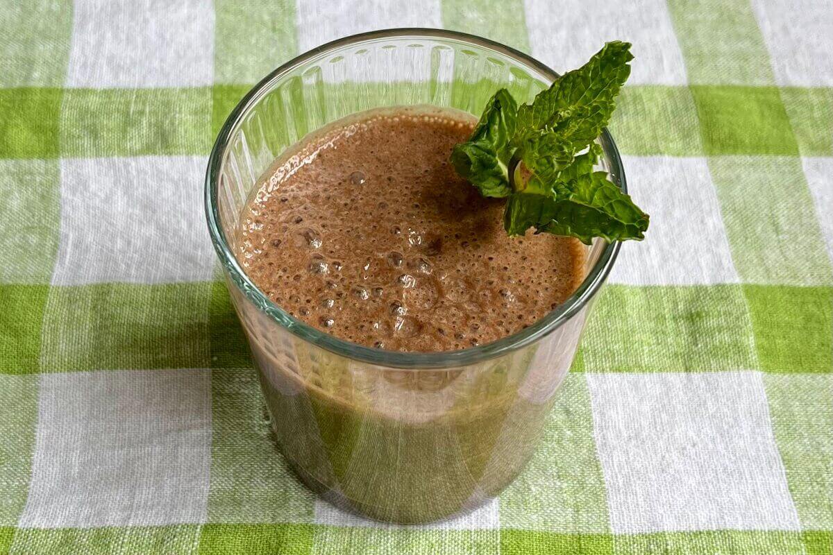 A mint chocolate smoothie in a glass with a sprig of fresh mint.