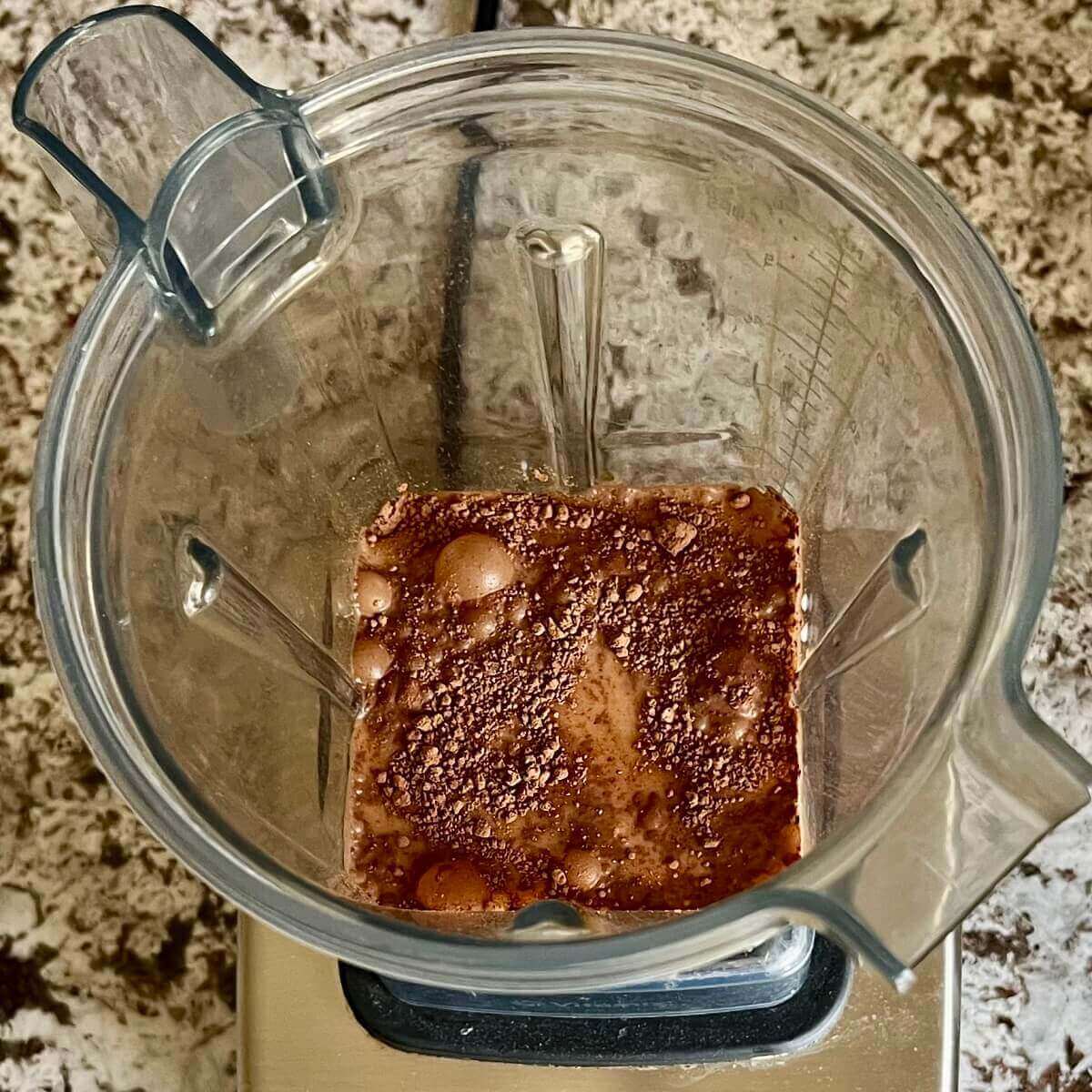 Orange, cocoa powder, and other ingredients for a smoothie in a blender.