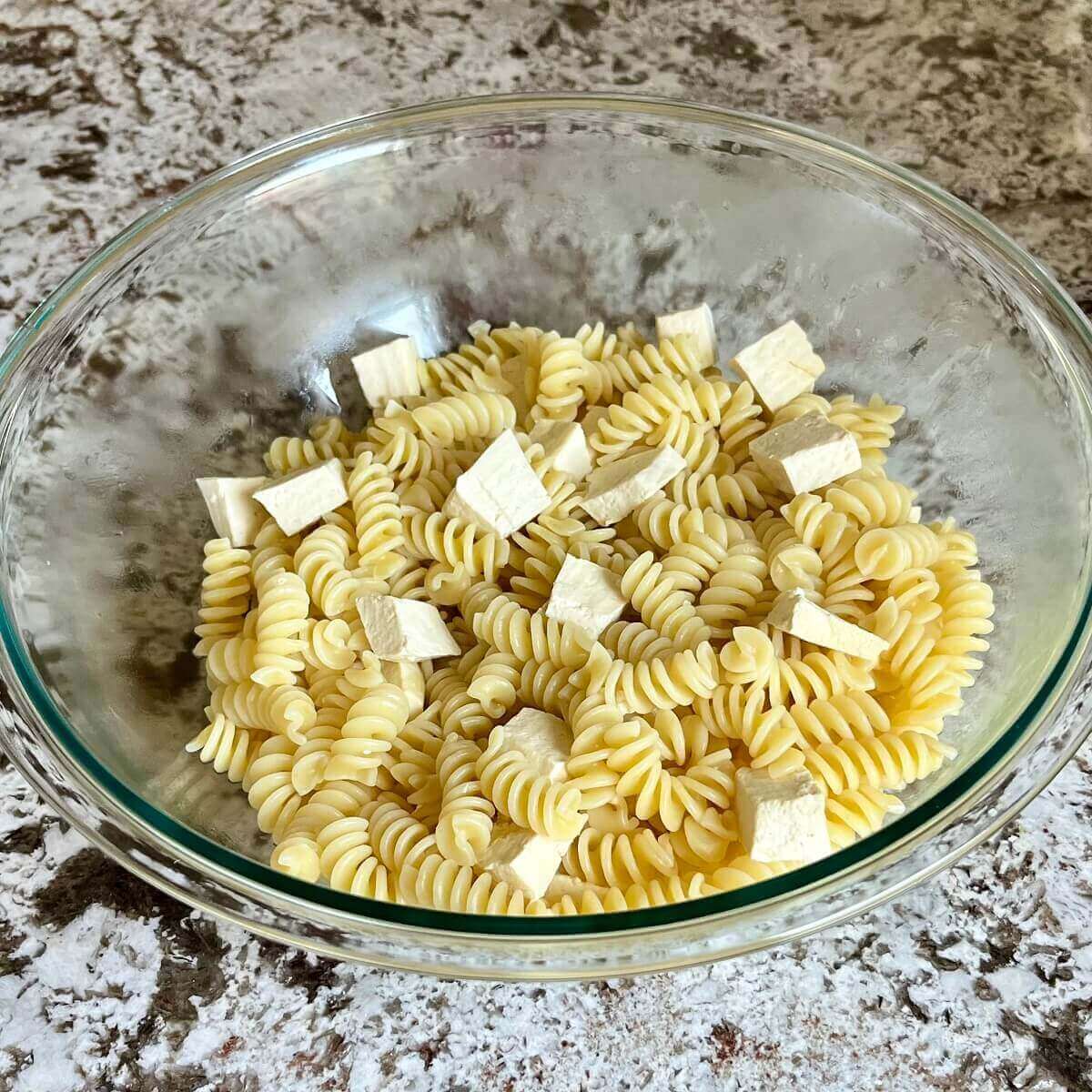 Pasta and chopped tofu in a glass mixing bowl.