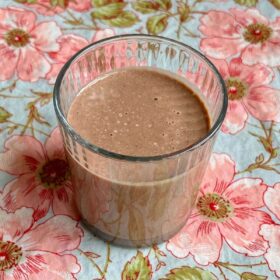 A pumpkin seed smoothie in a glass on a floral cloth.