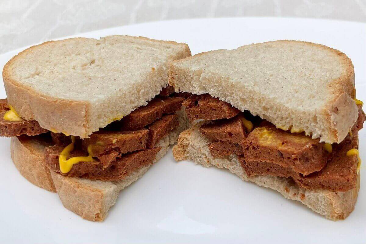 A plant-based pastrami sandwich on a white plate.