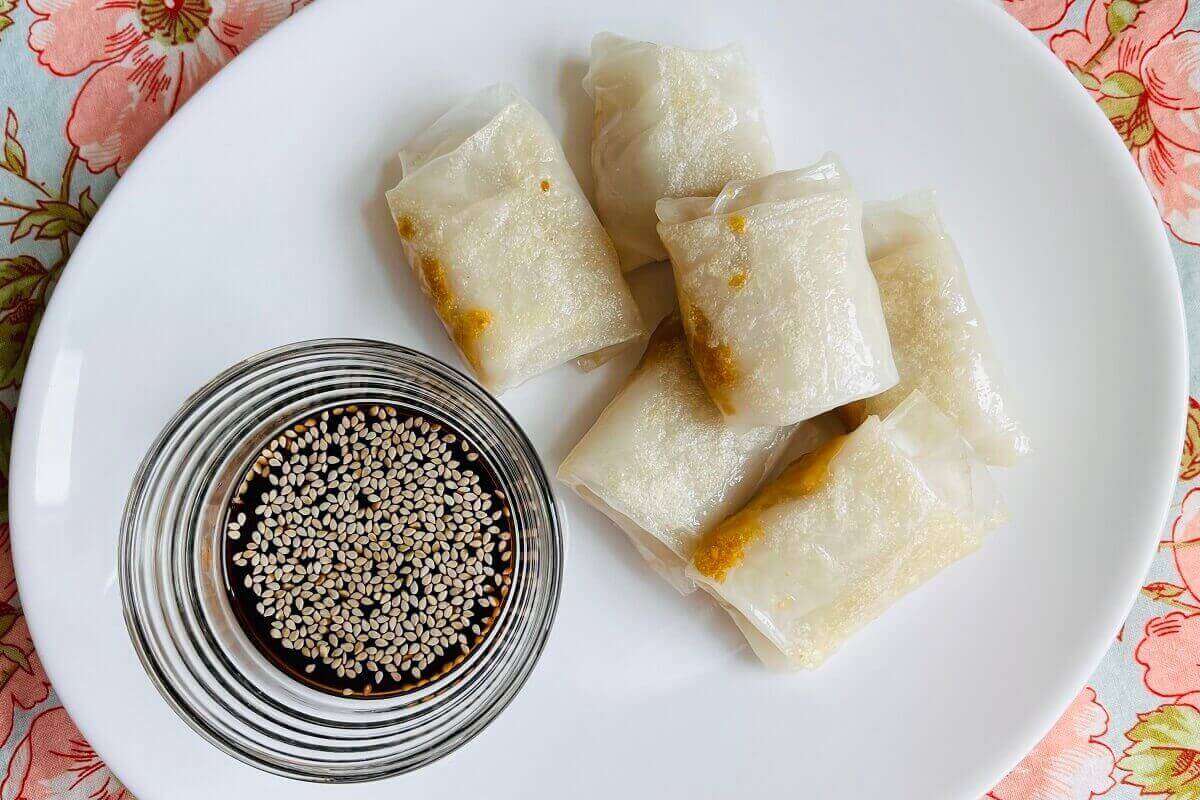 Six rice paper dumplings on a plate next to a bowl of dipping sauce.
