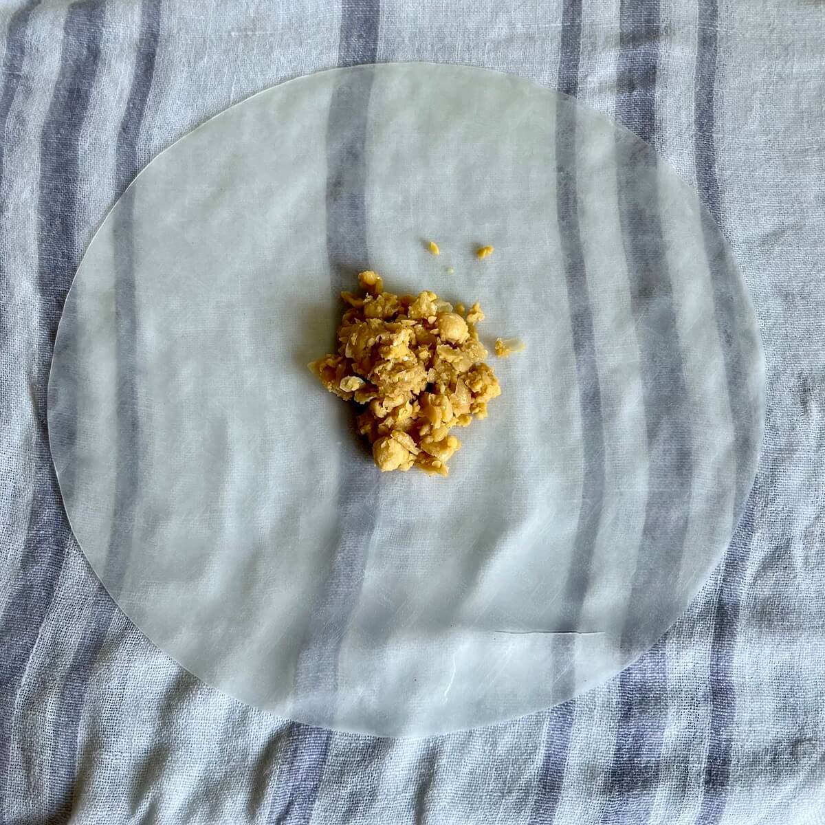 A scoop of chickpea filling on a sheet of rice paper on a damp kitchen towel.