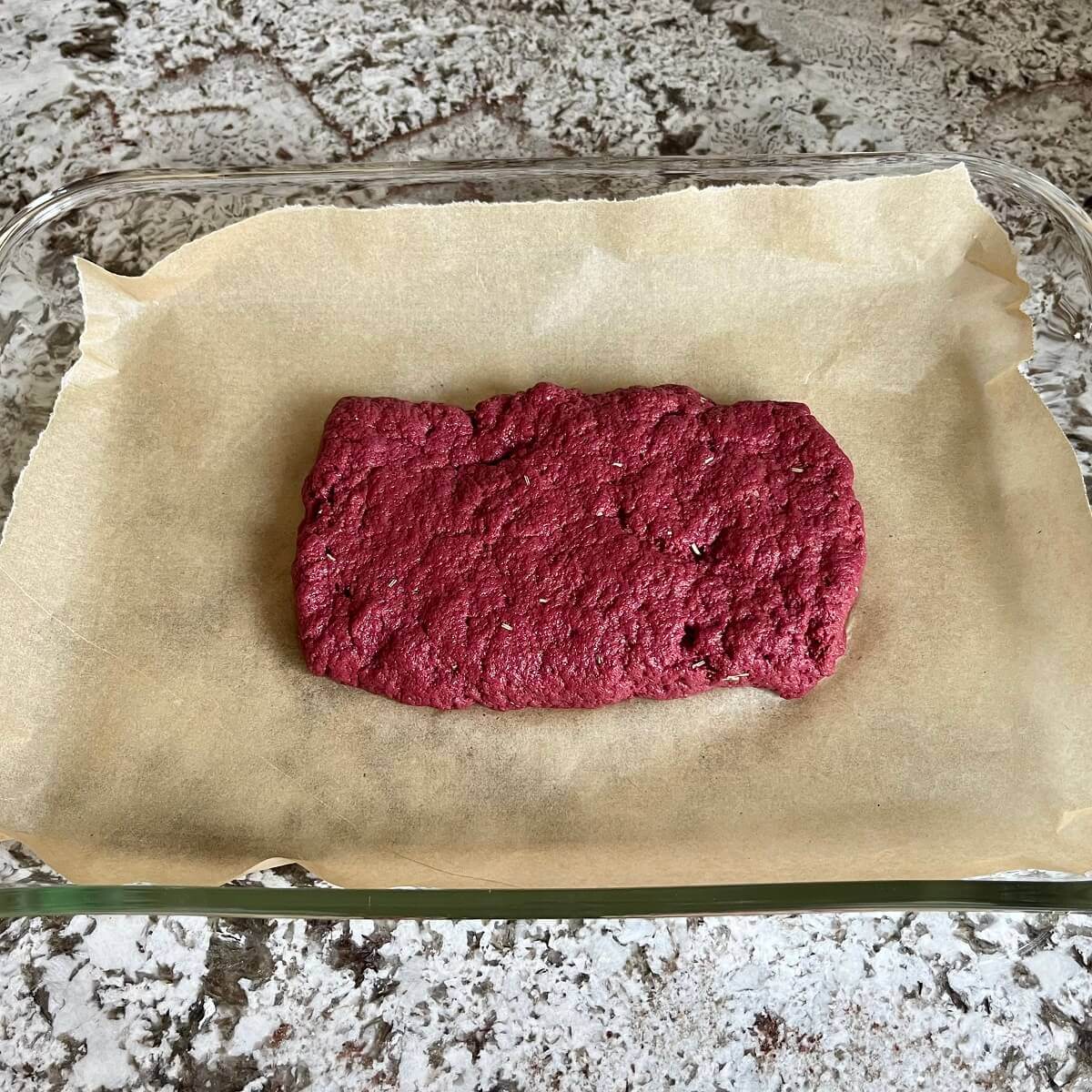 A loaf of raw seitan in a glass baking dish lined with parchment paper.