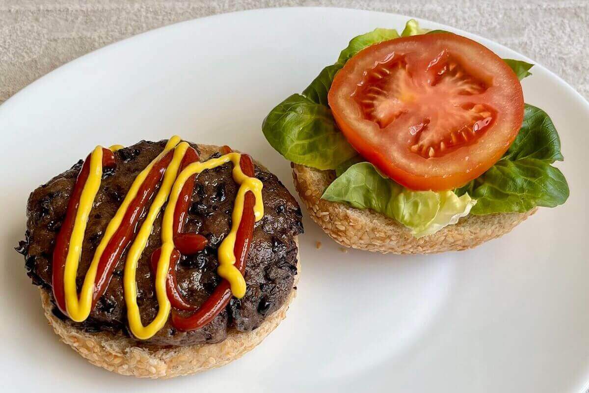 An open-faced vegan burger made with black beans on a white plate.