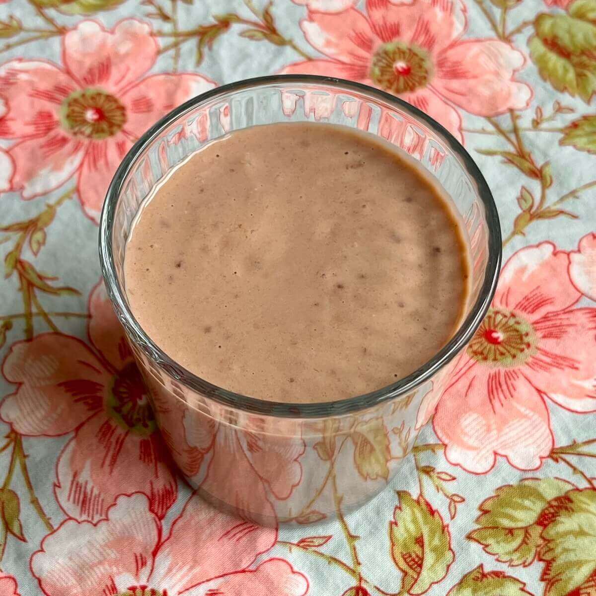 A vegan meal replacement smoothie in a glass on a floral cloth.