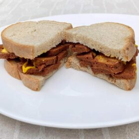 A vegan pastrami sandwich drizzled with mustard.