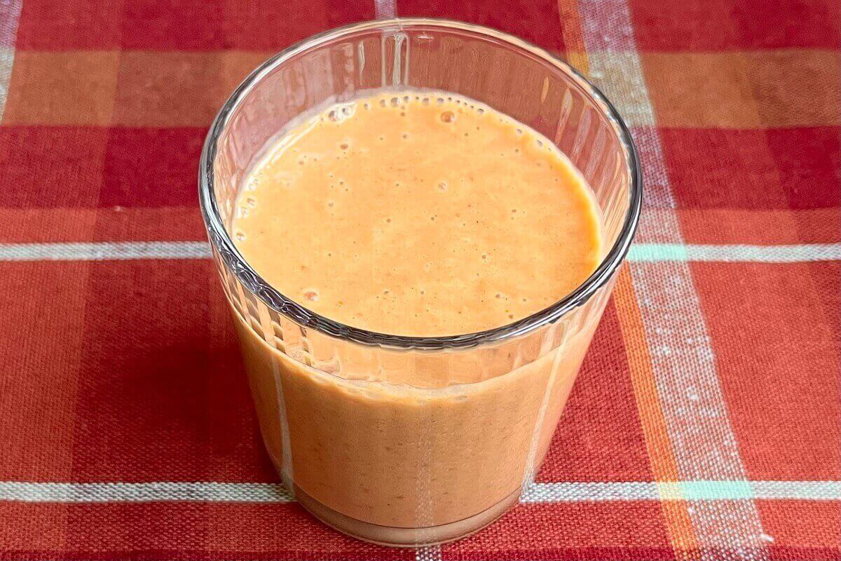A pumpkin spice smoothie in a glass on an orange plaid placemat.