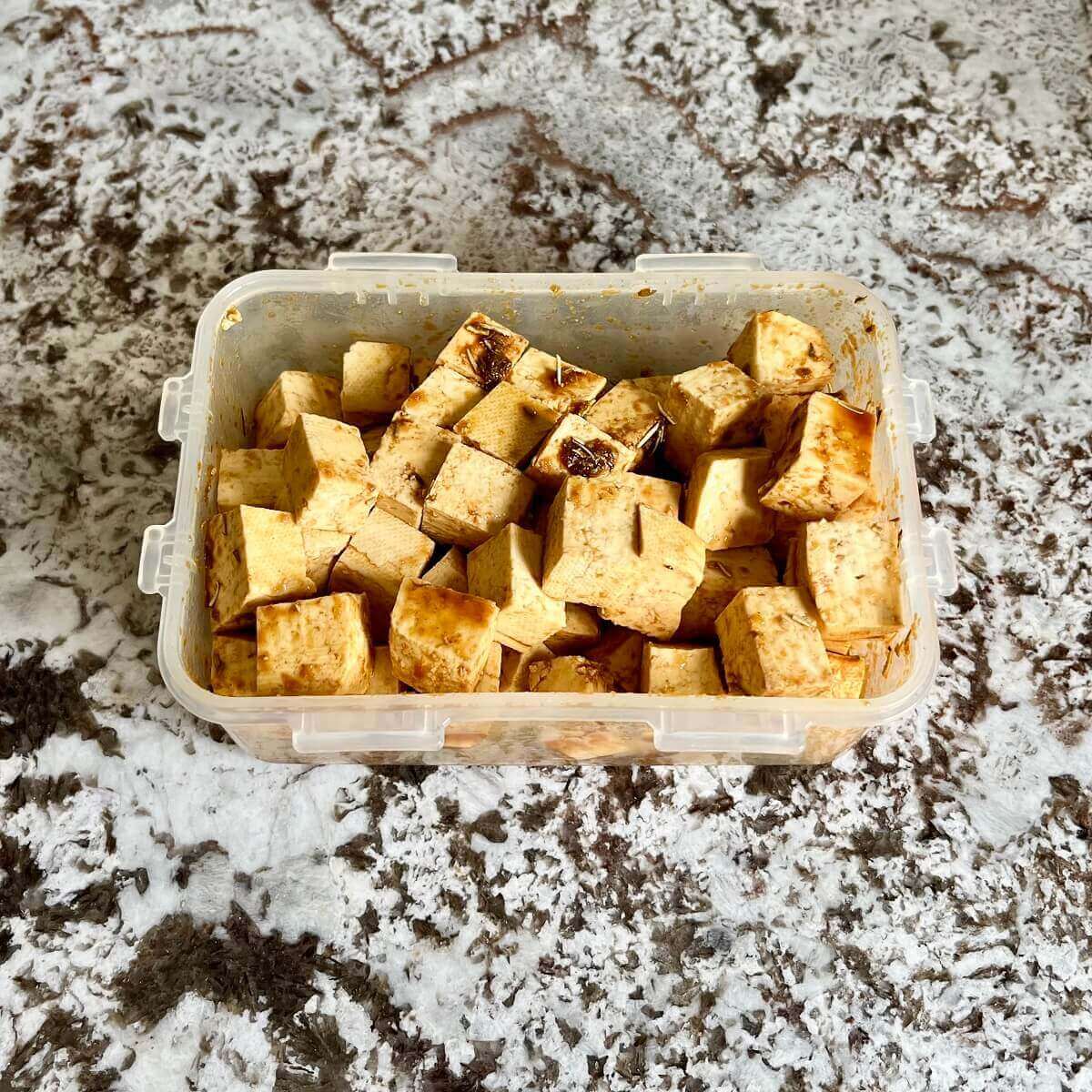 Tofu cubes marinating in a plastic container.